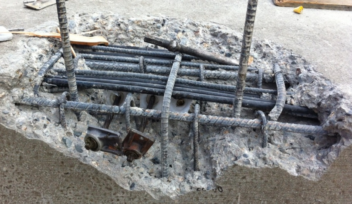 A severe concrete blowout in a post tension slab exposing the internal rebar and tendon anchors, caused by a void in the concrete pour.